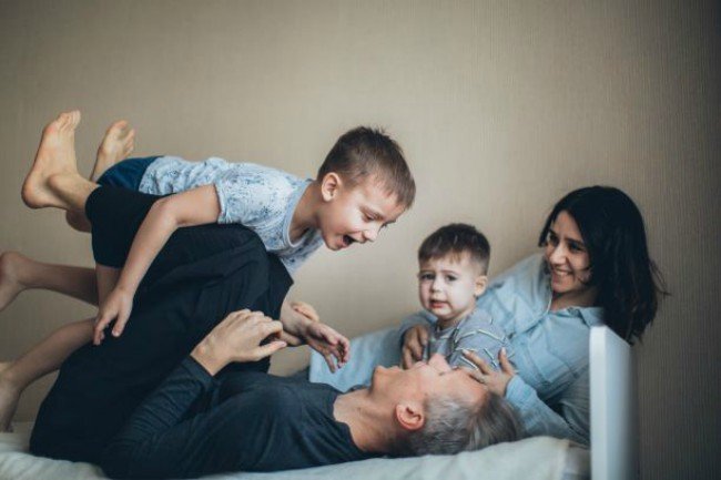 a family of four playing on the bed
